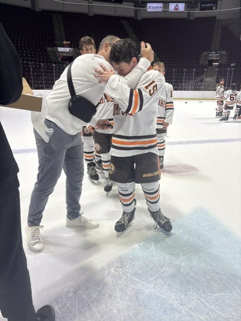 A Compuware player embraces his coach on the ice after the win